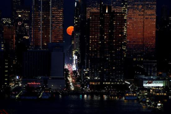 资料图：当地时间2018年6月28日，一轮猩红色的月亮从美国纽约曼哈顿世贸中心大楼后冉冉升起。繁华的城市、硕大的月亮，让人感觉仿佛看到了科幻大片中的场景。草莓月亮是指6月的满月，因为美国原住民认为这是采摘草莓的最佳时机。